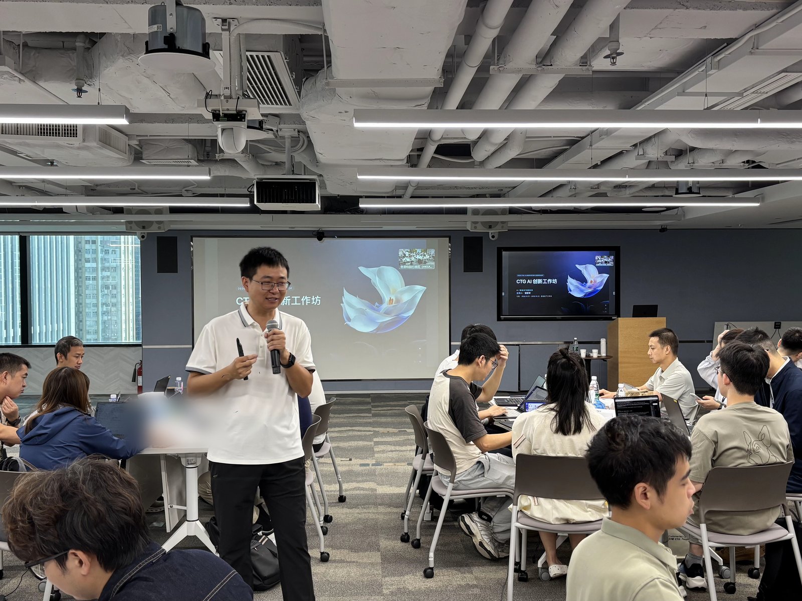 张财华在客户香港办公室主持 AI 创新工作坊，手持麦克风站在投影幕前